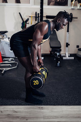 Fototapeta na wymiar Black sporty young man working out with sandbag while exercises in the gym. Attractive athletic male doing hard workout with weight training. Sport.