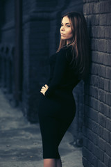 Young fashion woman in black dress leaning on brick wall