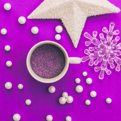 Obraz na płótnie Canvas Creative Christmas cup of hot violet unicorn drink among white shiny star, snowflake and balls decoration for tree on vibrant purple background. Happy holidays