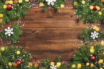 Fototapeta na wymiar Christmas frame greeting card. Branches of green Christmas spruce on a brown wooden background with red balls, snowflakes. Christmas lights garlands, snow on the brown wooden boards with place for you