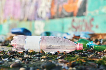 Spilled seaport garbage by the sea of a big city. Empty used dirty plastic bottles. Large amount urban rubbish. Dirty pier city port. Environmental pollution. Ecological problem. Bokeh city buildings