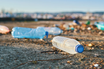 Spilled seaport garbage by the sea of a big city. Empty used dirty plastic bottles. Large amount urban rubbish. Dirty pier city port. Environmental pollution. Ecological problem. Bokeh city buildings