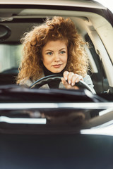 Fototapeta na wymiar portrait of beautiful cheerful ginger curly woman driving car