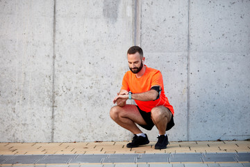 Sporty young man crouching and setting timer on wristwatch. Healthy lifestyle concept.