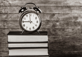 Alarm clock and books on wooden table. Image in black and white color style