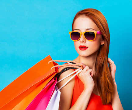 Style redhead woman holding shopping bags on blue background.