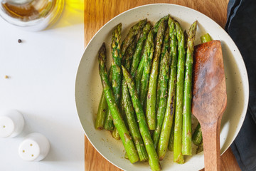 Top view on roasted asparagus in a white pan on a kitchen table. Modern style, vegetarian food.