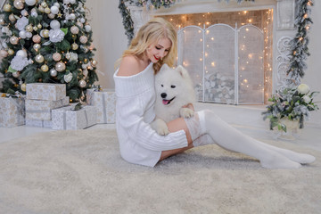 beautiful blonde in white clothes with a white husky on the background of the fireplace and Christmas tree.