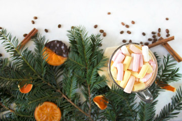 holidays, winter and celebration concept - hot chocolate drink with marshmallows, cinnamon, dry oranges, coffee beans and fir tree on white background. Winter christmas holiday background. Flat lay