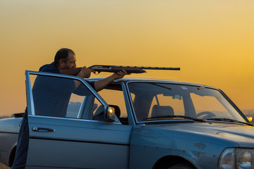 The guy shoots cartridges with a gun in nature, The hunter shoots at the target at sunset
