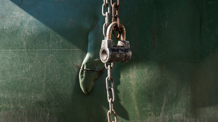 Old metal lock with a chain on green plastic background.