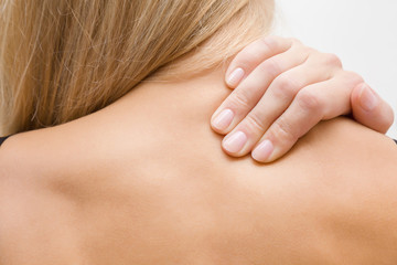 Young, blonde woman massaging her naked shoulder with hand. Pain from strain and incorrect posture....