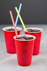 Three red cups with soda and colored straws on a gray background