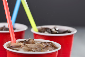 fizzy drink with ice in red cups with colored straws