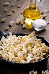  Prepared popcorn in frying pan, corn seeds in bowl and corncobs on kitchen table.Air salty...