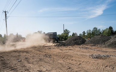 A truck with stones in the trailer moves along the way, picking up a dust.
