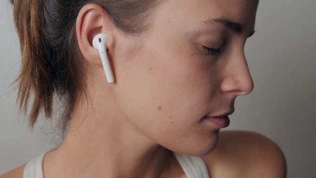 Portrait of a beautiful young, in a leather jacket with airpods in her ear, listens to music. Student dancing happy earpods handsfree bluetooch girl smiling, looking down.