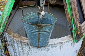 one gray metal bucket of water stands on an open well in the street