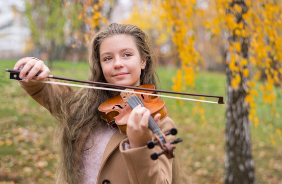 Girl playing the violin in the autumn park at a yellow foliage background.