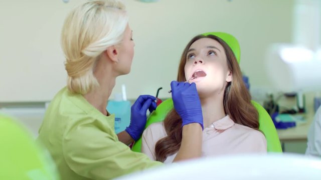 Regular dental checkup at professional dentist office. Happy woman on dental chair. Female dentist examining patient teeth with mouth mirror. Woman dentist with thumb up gesture