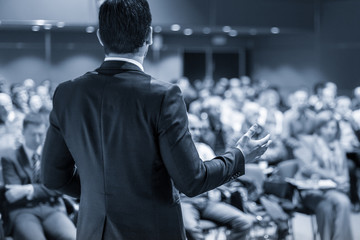 Speaker giving a talk on corporate business conference. Unrecognizable people in audience at...
