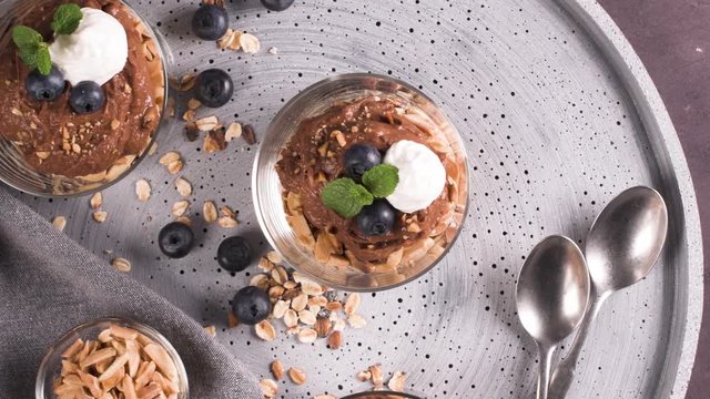 Glass cups of chocolate and chestnuts mousse with roasted almonds and oats decorated with black berries and mint leaves.
