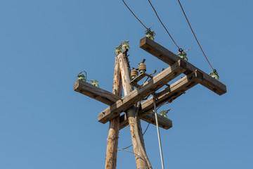 Old wooden pole and post with electrical power line against background of blue sky