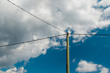 Old wooden pole and post with electrical power line against background of cloudy sky