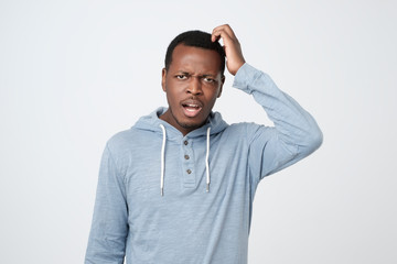 Young african man in blue shirt thinking scratching head on white background