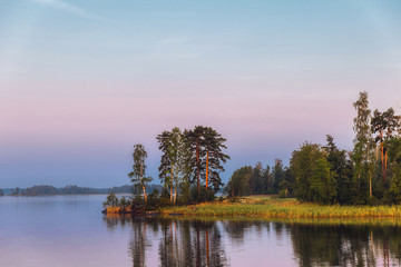 Obraz premium Bright island on a lake with pine trees in morning light