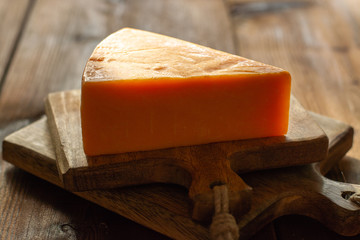 Piece of bright yellow hard cheese cheddar, originating in the English village of Cheddar in Somerset
