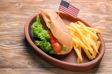 Tasty hot dog with American flag and french fries on plate