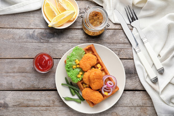Plate with delicious waffle and chicken nuggets on wooden table