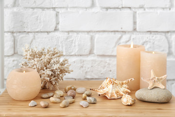 Seashells, pebbles and burning candles on table near white brick wall