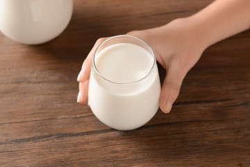 Female hand with glass of tasty milk on wooden table