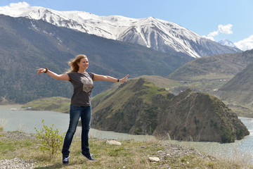 A young woman is balancing on her toes and smiling with pleasure among the snowy mountains.