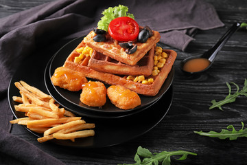 Delicious waffles with chicken nuggets and french fries on dark wooden table