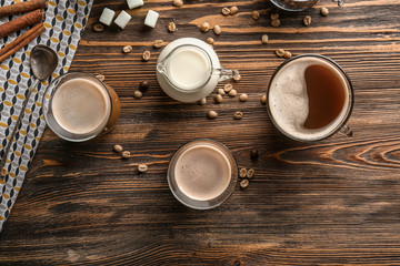 Glasses of tasty aromatic coffee with jug of milk and beans on wooden table