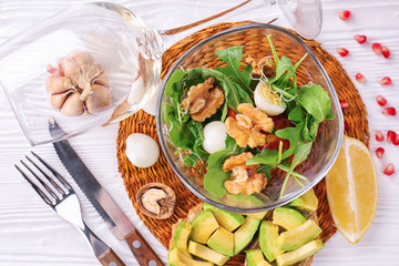Delicious fresh salad with walnuts in glass bowl on white table