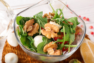 Delicious fresh salad with walnuts in glass bowl on table