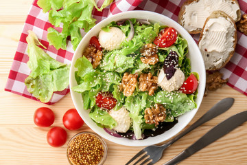 Delicious fresh salad with walnuts in bowl on wooden table