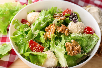 Delicious fresh salad with walnuts in bowl on wooden table, closeup