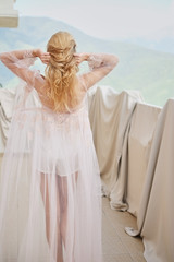 Fototapeta na wymiar silhouette of young beautiful girl bride in a peignoir stands of the balcony overlooking the mountains