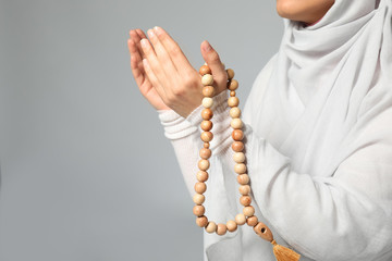 Young Muslim woman with rosary beads praying on light background, closeup