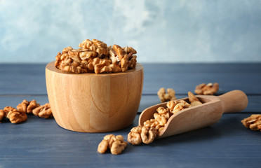 Bowl and scoop with tasty walnuts on color wooden table