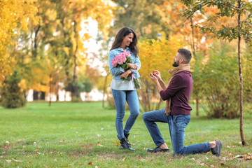 Young man proposing to his beloved in autumn park - obrazy, fototapety, plakaty