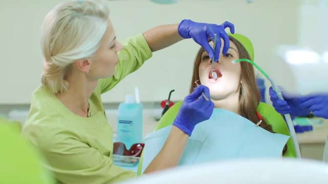 Dentist examining patient teeth with dental tools. Doctor and patient in modern dental clinic interior. Professional oral hygiene procedures on dental chair. Saliva ejector in opened patient mouth