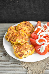 Chicken breasts coated with cheese, tomatoes on white plate, on old wooden table