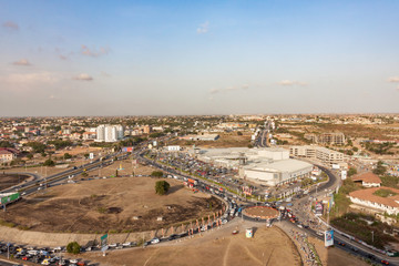 High view point cityscape of Accra, Ghana. Traffic jam on a roundabout at a shopping mall next to an highway interchange. The slums houses and buildings of Northern Accra on the background.
