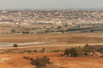 High view point cityscape of Accra, Ghana. Airplane flying low for landing.  With a neighbourhood behind the Kotoka International Airport sandy wasteland landing strip. Hazy sea with ships on horizon